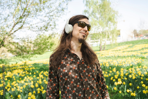 Smiling man with long hair wearing sunglasses listening to music at daffodil meadow photo