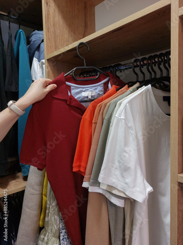 Side view of woman choosing clothes on hangers in wooden wardrobe with various garments
