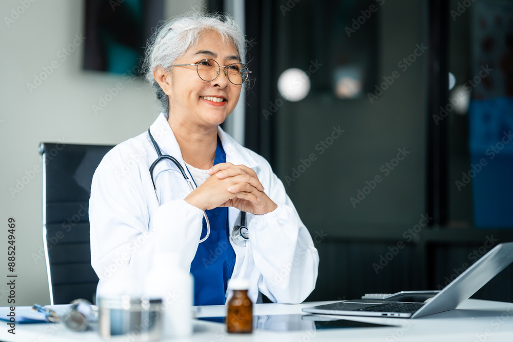 A grey-haired Asian mature woman nurse, doctor, disease specialist, and surgeon works at a desk, utilizing her expertise as an experienced and senior healthcare professional. A grey-haired Asian mature woman nurse, doctor, disease specialist, and surgeon works at a desk, utilizing her expertise as an experienced and senior healthcare professional.