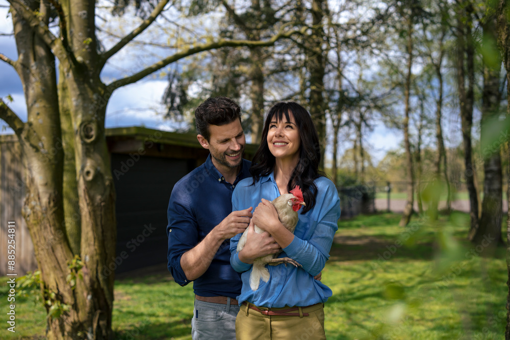 Happy businessman with businesswoman holding rooster chicken in back yard garden Happy businessman with businesswoman holding rooster chicken in back yard garden