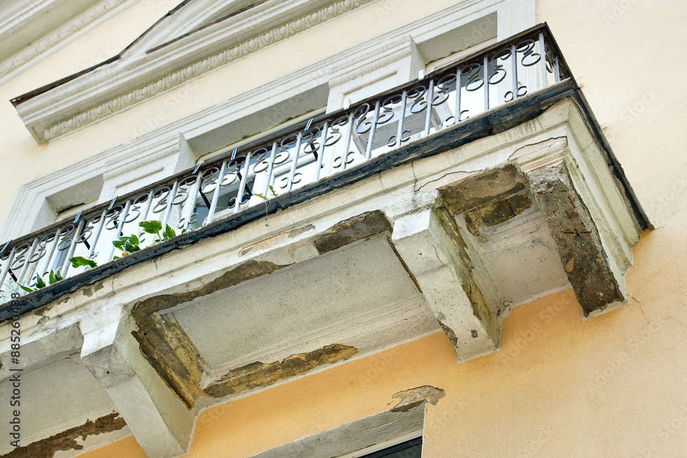 Obraz premium Damaged balcony of an old historic building. Broken balcony floor, cracked concrete and plaster, rusty bars and reinforcement. Emergency balcony repair, cracks in reinforced concrete structure