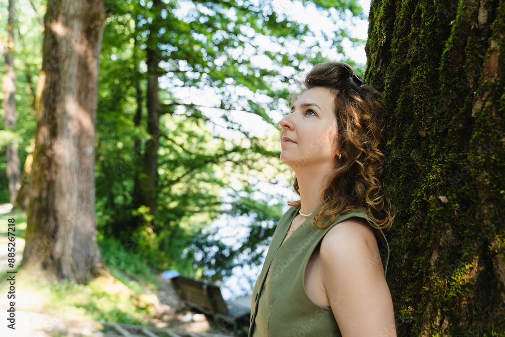 Thoughtful woman leaning on tree in park Thoughtful woman leaning on tree in park