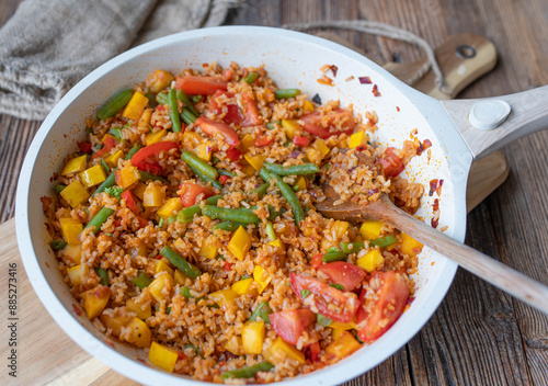 Healthy vegetable rice cooked with brown rice, zucchini, green beans, tomatoes, onions, and garlic in a frying pan