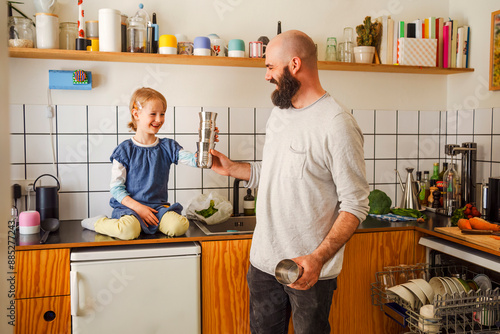 Smiling father playing with daughter sitting on kitchen counter at home photo