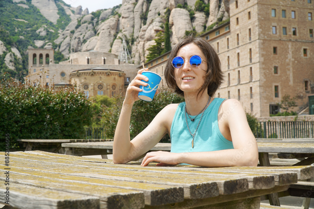 Young woman tourist drinking a coffee on the grounds of Santa Maria Abbey in the mountains of Montserrat near Barcelona, Spain