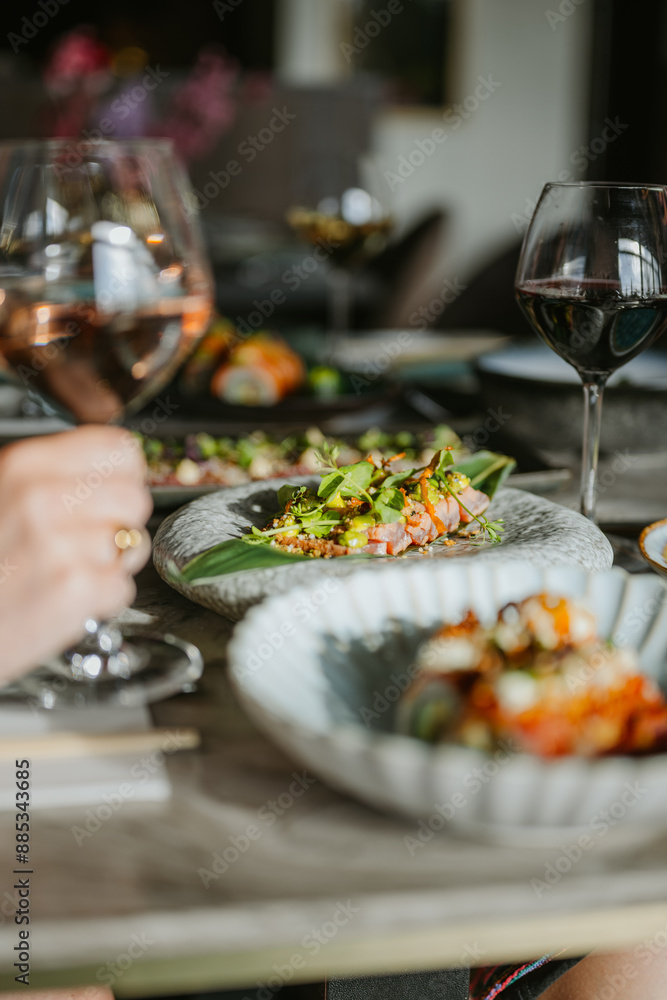 Closeup shot of sushi on multiple plates and people holding glasses of wine Closeup shot of sushi on multiple plates and people holding glasses of wine