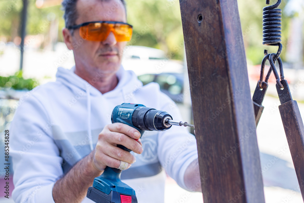 Naklejka premium Man in protective eyewear using power drill outdoors