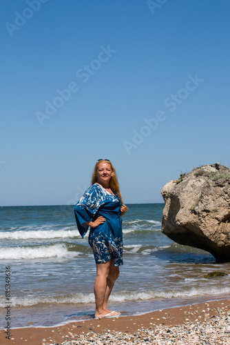 A woman in a blue tunic stands against the background of a blue sea. Sea, vacation on the beach