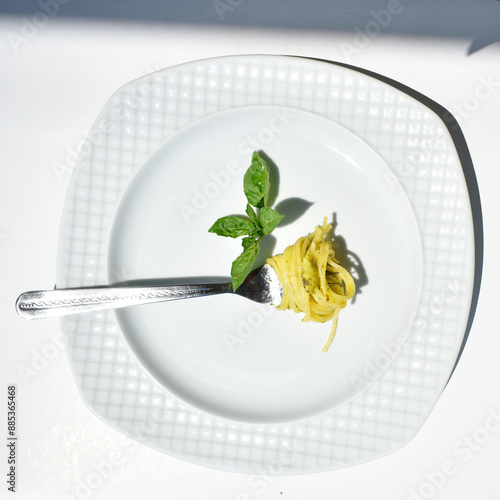 Fotografia Spaghetti wrapped on a fork, on a white plate, decorated with a basil leaf, top