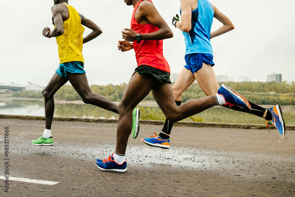 three runners dressed in bright sports clothes race along calm river, summer marathon three runners dressed in bright sports clothes race along calm river, summer marathon