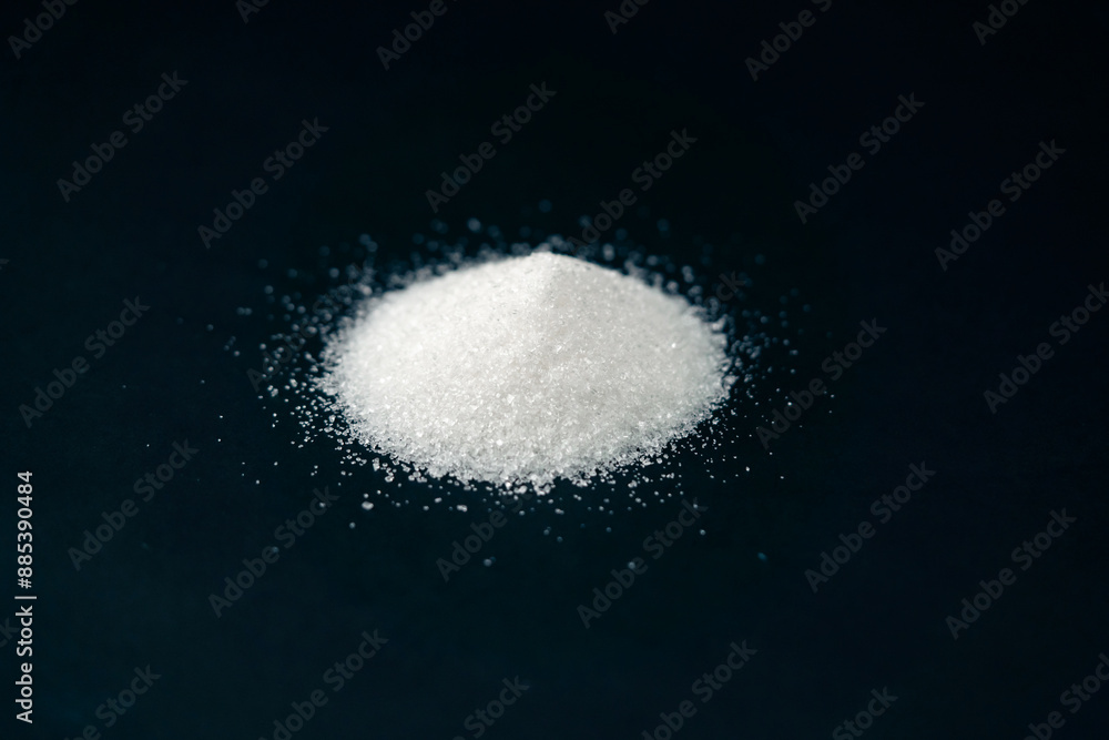 Fototapeta premium close-up on a black-blue background white crumbly granulated sugar lies on it, crystal lumps around a pile of sugar are harmful to health