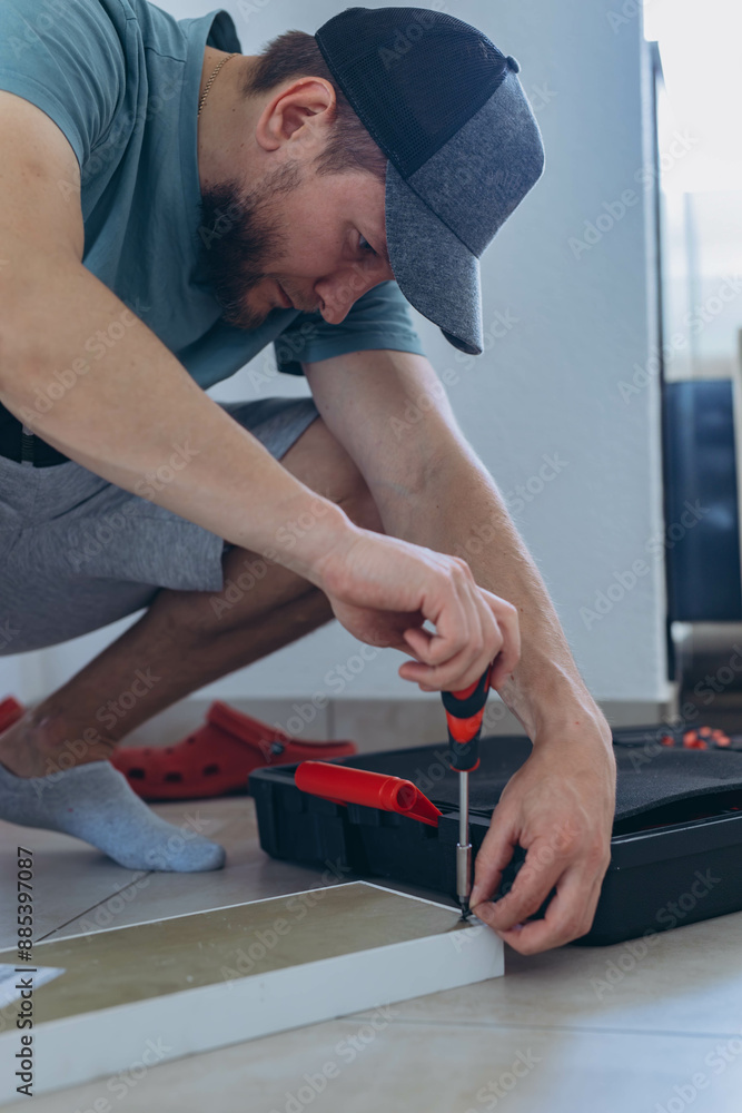 Close-up of a man's hands screwing screws into a wooden shelf on the floor using a screwdriver Close-up of a man's hands screwing screws into a wooden shelf on the floor using a screwdriver
