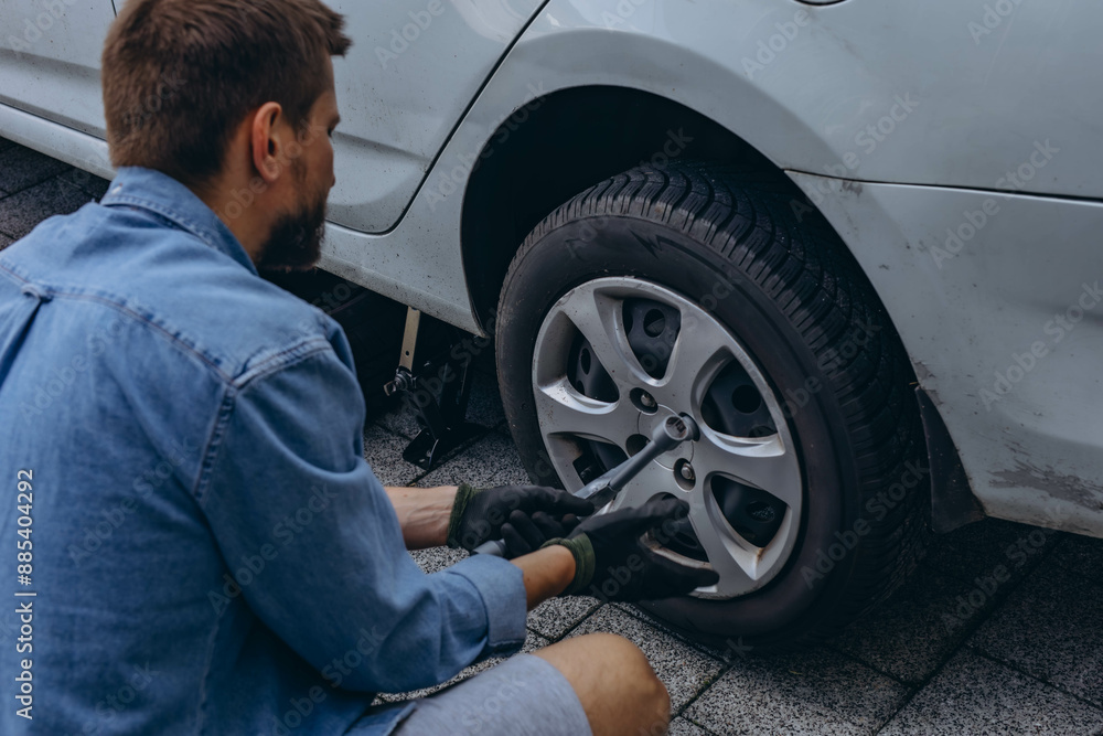 Young man in unscrewing lug nuts on car wheel in process of new tire replacement,using wrench while changing flat tire on the road. Young man in unscrewing lug nuts on car wheel in process of new tire replacement,using wrench while changing flat tire on the road.