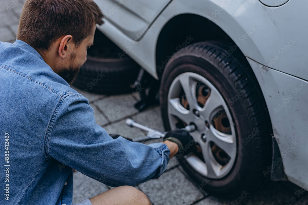 Young man in unscrewing lug nuts on car wheel in process of new tire replacement,using wrench while changing flat tire on the road. Young man in unscrewing lug nuts on car wheel in process of new tire replacement,using wrench while changing flat tire on the road.