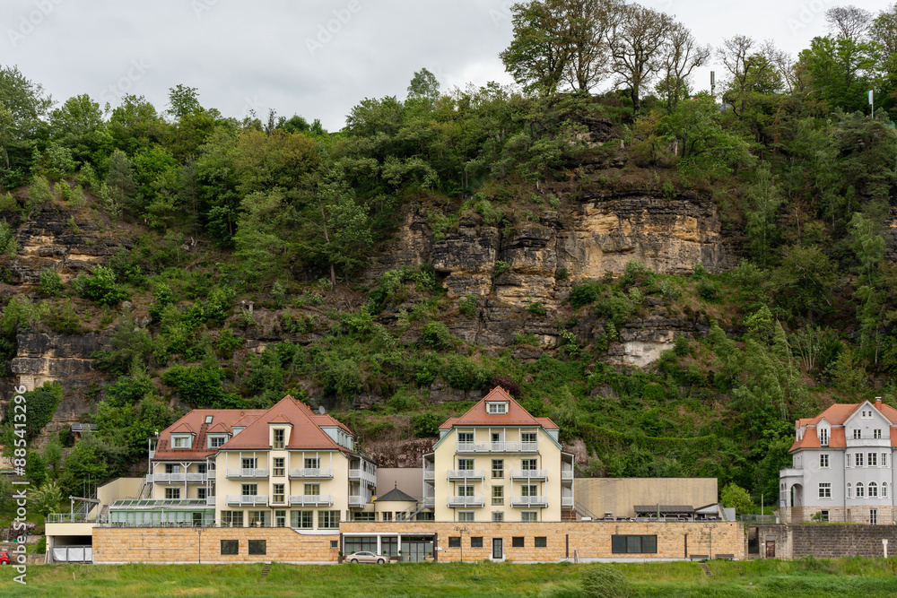 A row of houses with a large hill in the background. The houses are all different sizes and styles, but they all have a similar color scheme. The hill is covered in lush green trees A row of houses with a large hill in the background. The houses are all different sizes and styles, but they all have a similar color scheme. The hill is covered in lush green trees