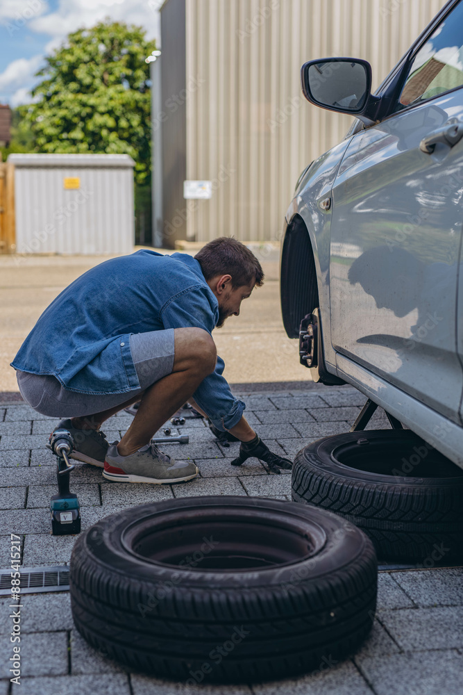 Young man in unscrewing lug nuts on car wheel in process of new tire replacement,using wrench while changing flat tire on the road. Young man in unscrewing lug nuts on car wheel in process of new tire replacement,using wrench while changing flat tire on the road.