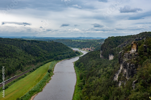 A river flows through a lush green valley with a train passing by. The scene is serene and peaceful, with the train adding a sense of movement and life to the landscape