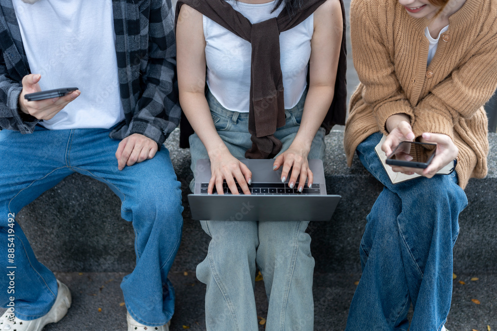 Fototapeta premium Three people sitting on a bench with a laptop and cell phones