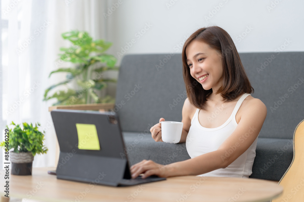 Woman working from home on a laptop, drinking coffee, and smiling. Comfortable workspace with natural light and greenery in the background. Woman working from home on a laptop, drinking coffee, and smiling. Comfortable workspace with natural light and greenery in the background.