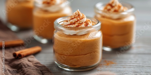 Fototapeta Naklejka Na Ścianę i Meble -  Homemade creamy pumpkin spice mousse topped with whipped cream in glass jars, perfect for a cozy fall dessert. Cinnamon sticks included.