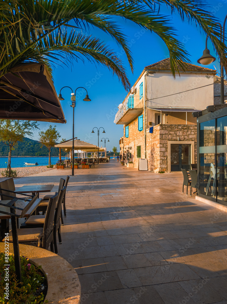 Primosten, Croatia - Beach promenade of Primosten old town on a sunny summer morning in Dalmatia with palm tree, restaurants, warm lights and blue sea water at the Adriatic sea coast