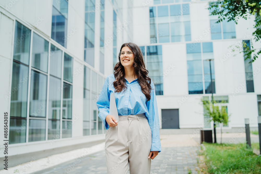 One beautiful young successful business woman going to work at business office modern building while holding papers and wearing glasses One beautiful young successful business woman going to work at business office modern building while holding papers and wearing glasses