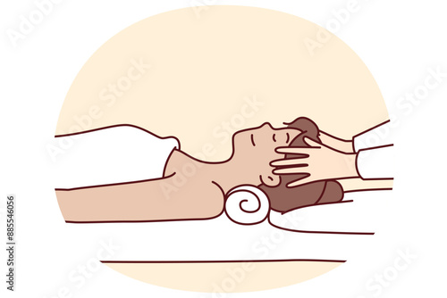 Woman in massage parlor lies on couch near hands of spa specialist doing facial rejuvenation procedure. Massage of head for getting rid of migraine and rejuvenating effect in cosmetology clinic
