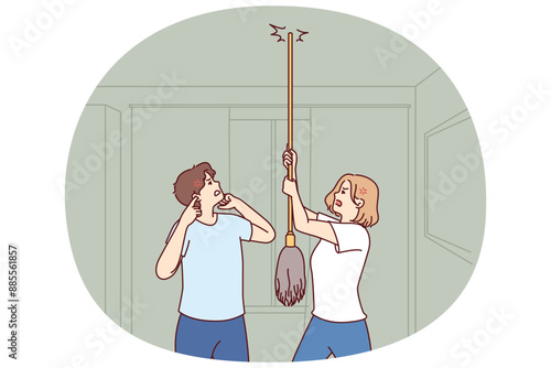 Young couple bangs on ceiling with mop urging neighbors to stop party or turn off loud music. Angry men and women use mop suffer from noisy neighbors not respecting rules of living together