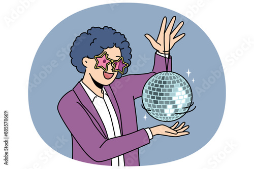 Funny man with disco ball with curly wig on head came to nightclub or dance floor to have fun and relax. Young guy enjoys atmosphere of music festival or disco party for party people