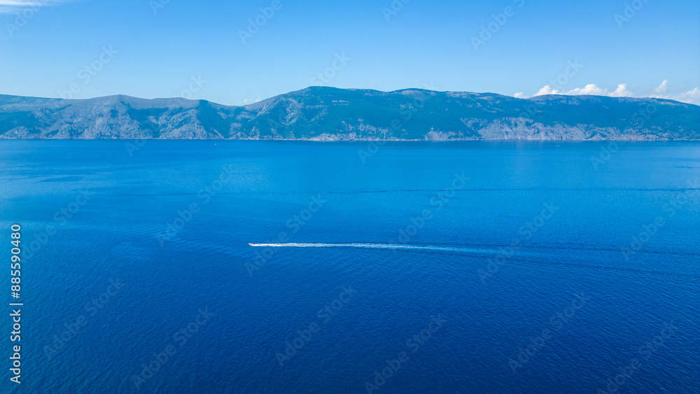 A serene and picturesque beach with turquoise waters, captured by drone on the island of Krk near Glavotok. This idyllic spot features lush trees lining the shore and a boat drifting on the deep blue A serene and picturesque beach with turquoise waters, captured by drone on the island of Krk near Glavotok. This idyllic spot features lush trees lining the shore and a boat drifting on the deep blue