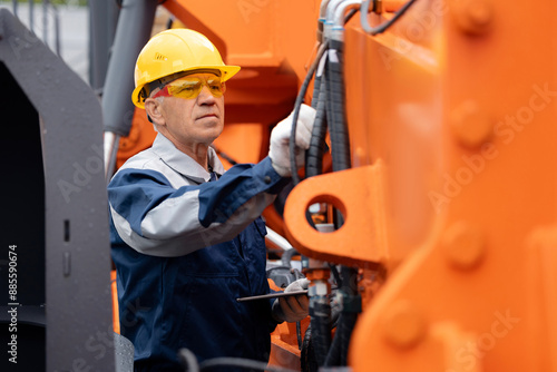 Mechanic repairing hydraulic hose in drilling machine, exploration drilling. Adult man in hard hat industrial worker. photo