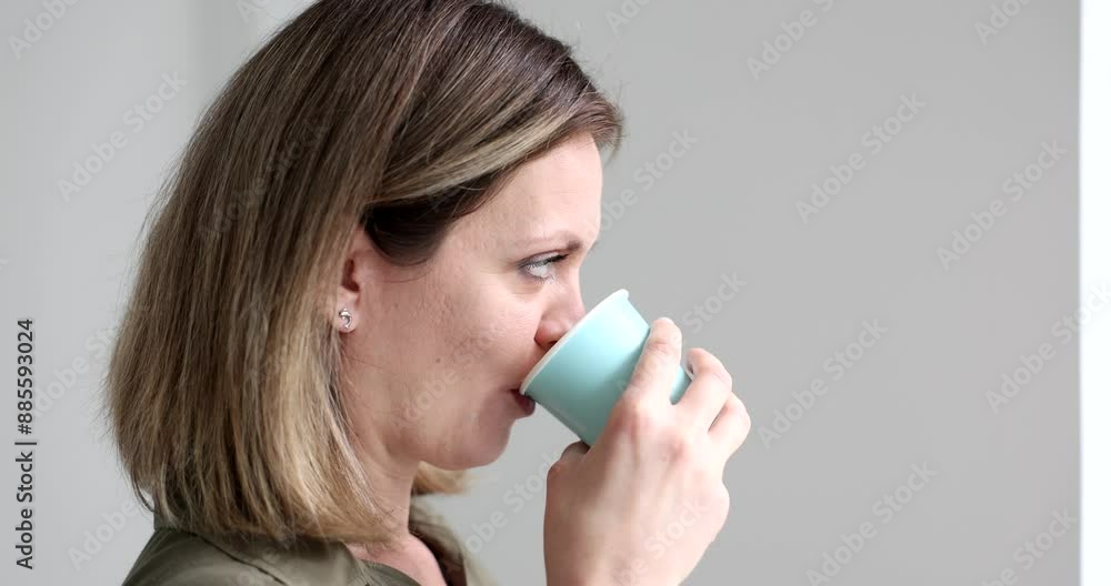 Serious woman drinks fresh water from paper cup in morning looking out window. Female employee quenches thirst standing on grey background slow motion Serious woman drinks fresh water from paper cup in morning looking out window. Female employee quenches thirst standing on grey background slow motion