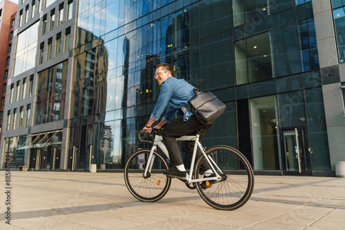 A smiling young man riding a bicycle past a modern glass office building, showcasing a vibrant and active urban lifestyle. © muse studio