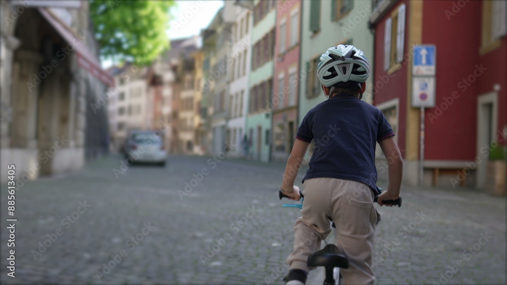 Obraz premium Child riding bicycle with helmet on cobblestone street in charming old town with colorful buildings, promoting outdoor activity and exploration in historic urban environment