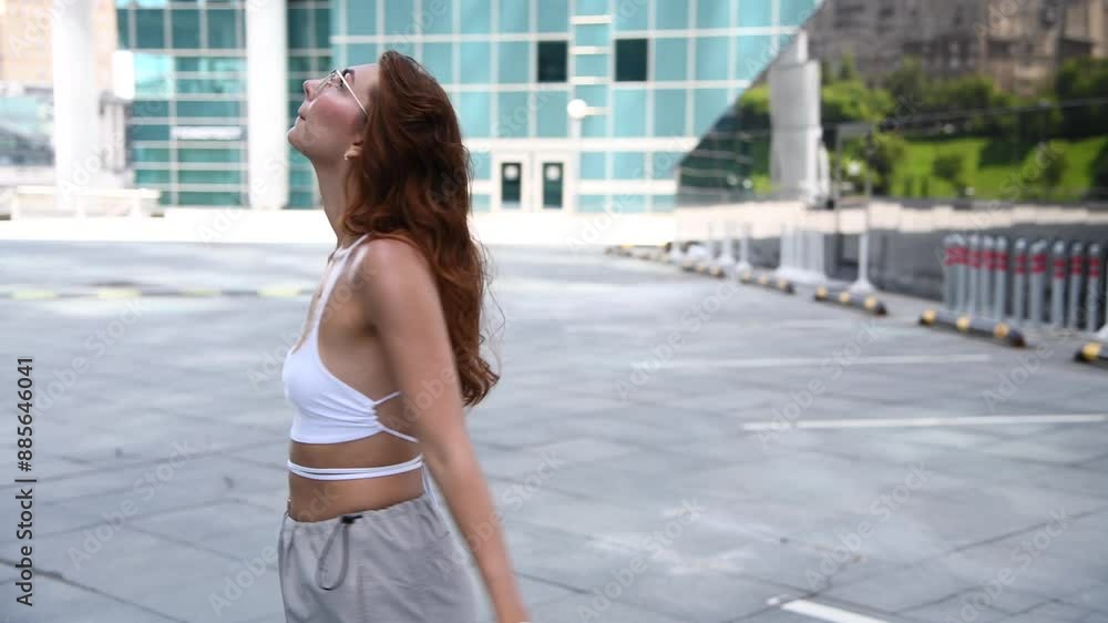 Portrait of beautiful long haired brunette woman in eyeglasses and hip hop streetwear standing by modern glass buildings and holding her smartphone and handbag on city street. Soft focus. Portrait of beautiful long haired brunette woman in eyeglasses and hip hop streetwear standing by modern glass buildings and holding her smartphone and handbag on city street. Soft focus.