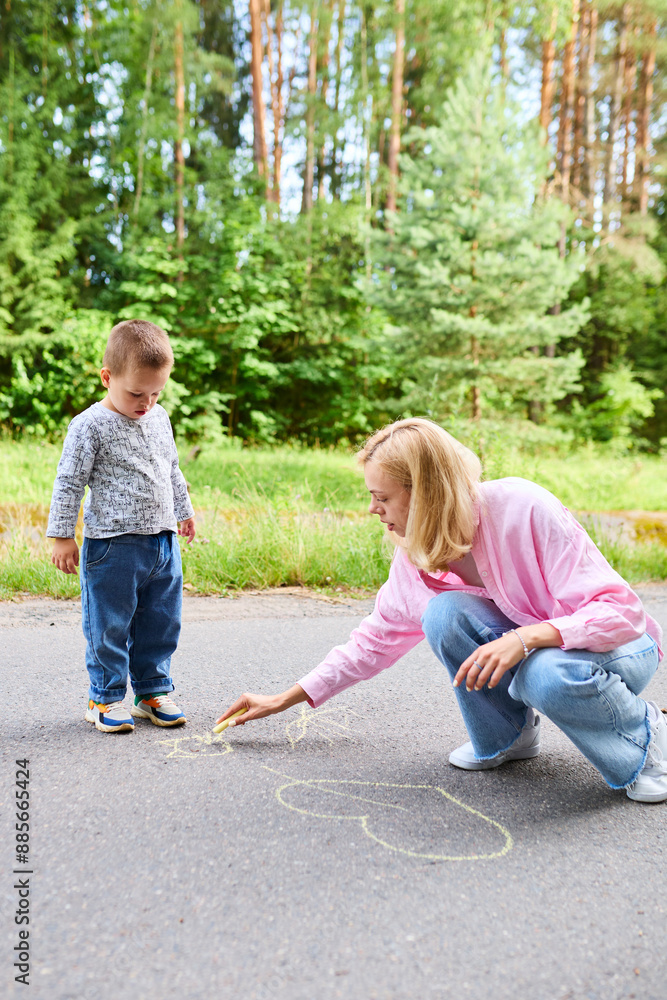 Fototapeta premium Motherhood concept. Mom and child have fun and draw on the asphalt