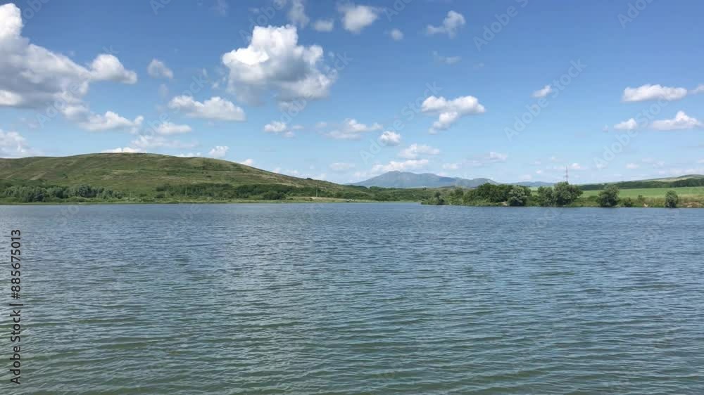 Serene Midday Lake Scene with Rolling Green Hills and Fluffy White Clouds Under a Clear Blue Sky Serene Midday Lake Scene with Rolling Green Hills and Fluffy White Clouds Under a Clear Blue Sky