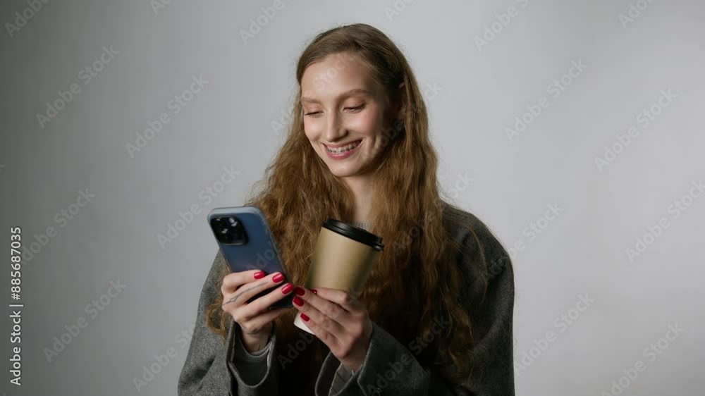 An attractive young woman with a cup of coffee and a smartphone on a light background An attractive young woman with a cup of coffee and a smartphone on a light background