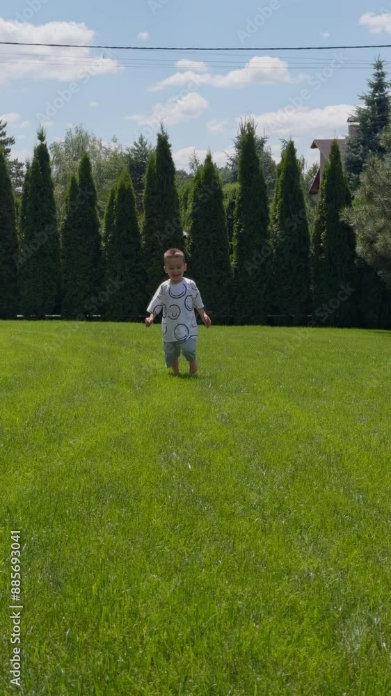Small male kid runs by the lawn approaching camera. Happy toddler pulls his pants as he runs and turns around in front of camera. Vertical video. Small male kid runs by the lawn approaching camera. Happy toddler pulls his pants as he runs and turns around in front of camera. Vertical video.