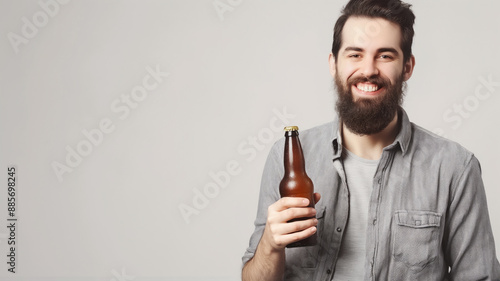 Bearded man in gray shirt smiling and holding a beer bottle against a light background. He looks content and ready to enjoy his drink