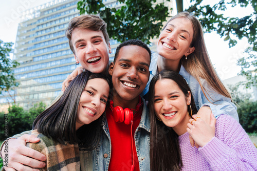 Group of teenage friends embracing together and looking at camera on a party. Excited young people having fun together on a meeting. Classmates posing for a photo. Joyful multiethnic guys smiling