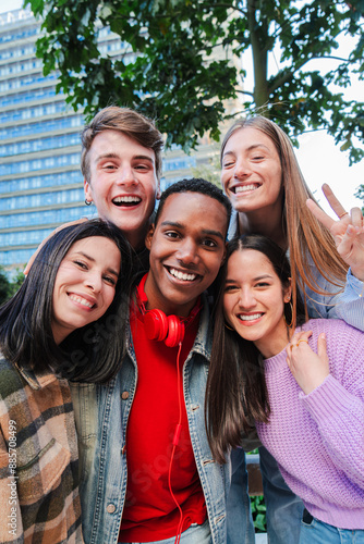 Vertical group of teenage friends embracing together and looking at camera on a party. Excited young people having fun together on a meeting. Classmates posing for a photo. Multiethnic guys smiling