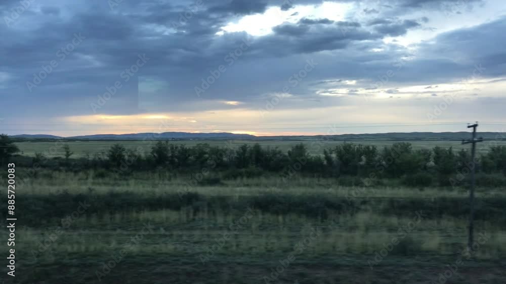 Scenic Sunset Over Rolling Plains Viewed from Train Window During Evening Journey Through Vast Countryside, Capturing Tranquil Sky with Storm Clouds and Distant Mountains Scenic Sunset Over Rolling Plains Viewed from Train Window During Evening Journey Through Vast Countryside, Capturing Tranquil Sky with Storm Clouds and Distant Mountains