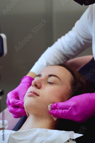 A beautician in pink gloves wipes a moisturizing mask from a girl's face with sponges