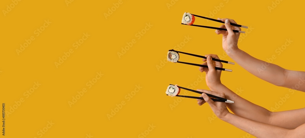 Hands holding chopsticks with different tasty sushi rolls on yellow background with space for text Hands holding chopsticks with different tasty sushi rolls on yellow background with space for text
