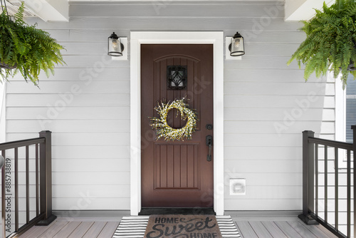 A wooden front door detail with grey vinyl siding, composite decking floor and raining, and lights mounted aside the doorway.