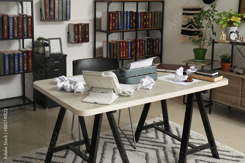 Vintage typewriter with crumpled paper sheets and books on table in office