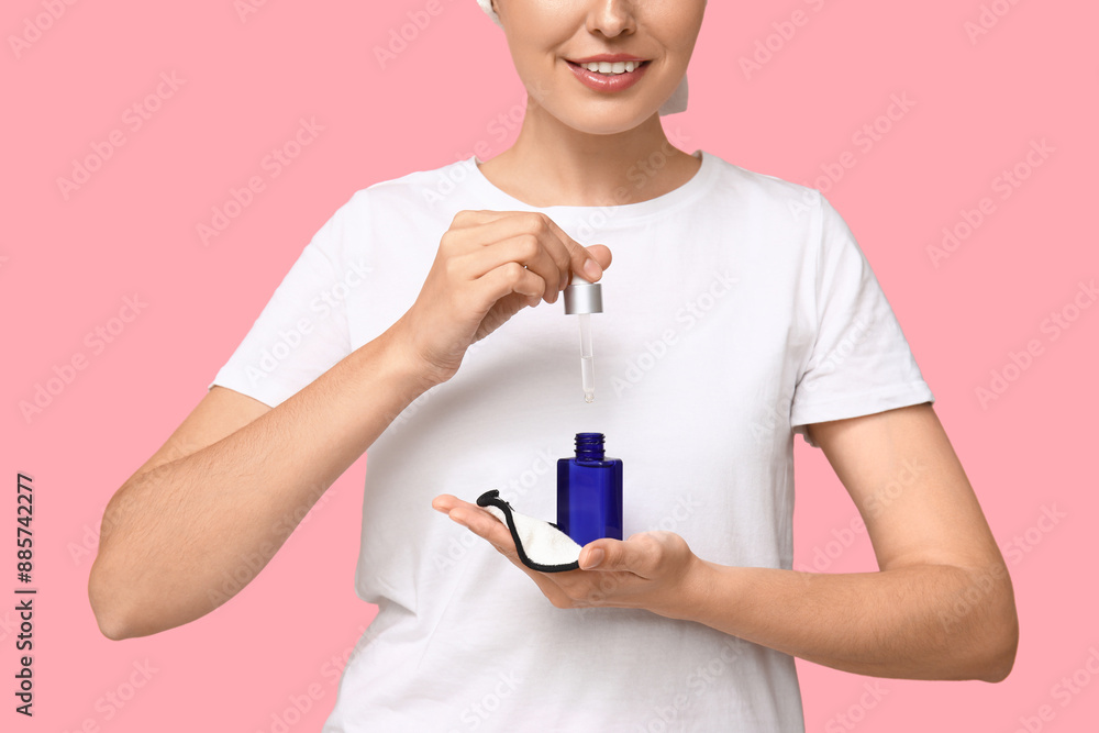Young woman with reusable cotton pad and dropper bottle on pink background, closeup