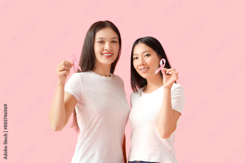 Young Asian women with pink ribbons on color background. Breast cancer awareness concept Young Asian women with pink ribbons on color background. Breast cancer awareness concept
