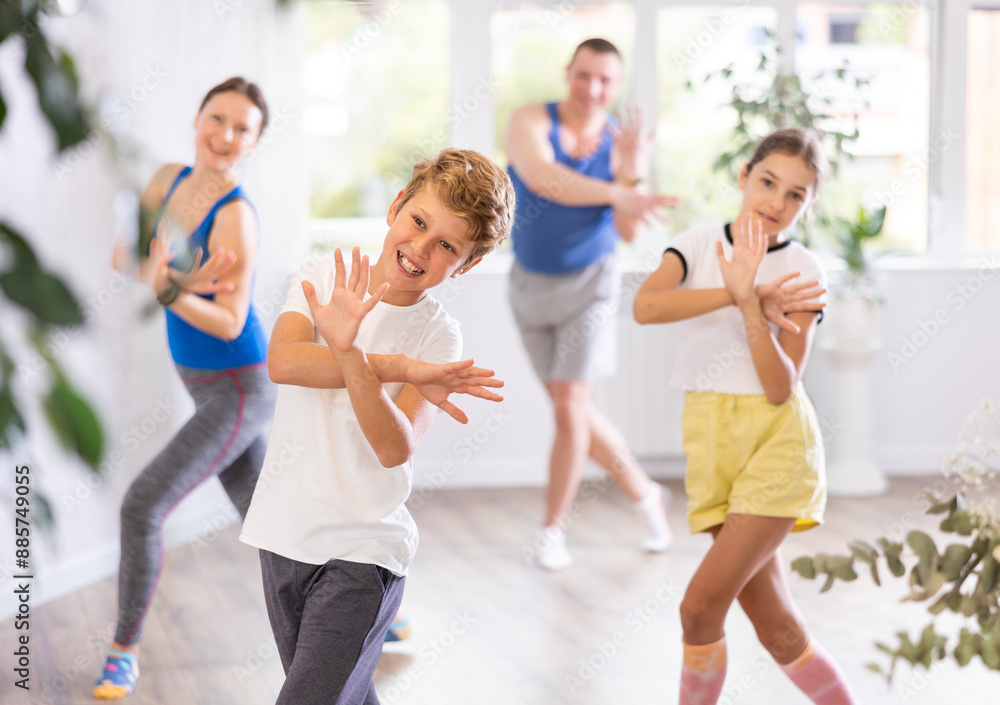 Obraz premium Excited preteen boy and girl exercising dance moves with their parents during dance class, family practicing dance with crossed hands in studio